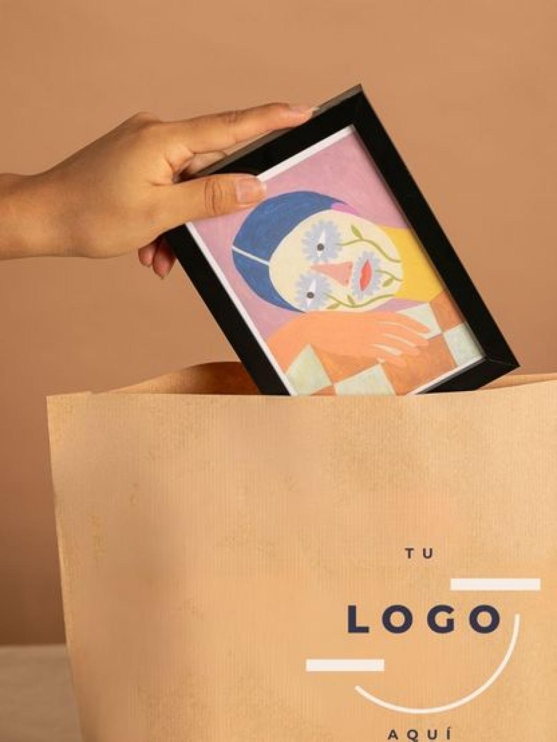 Mano introduciendo un marco con ilustración en una bolsa de papel kraft hexagonal grande personalizable con logo