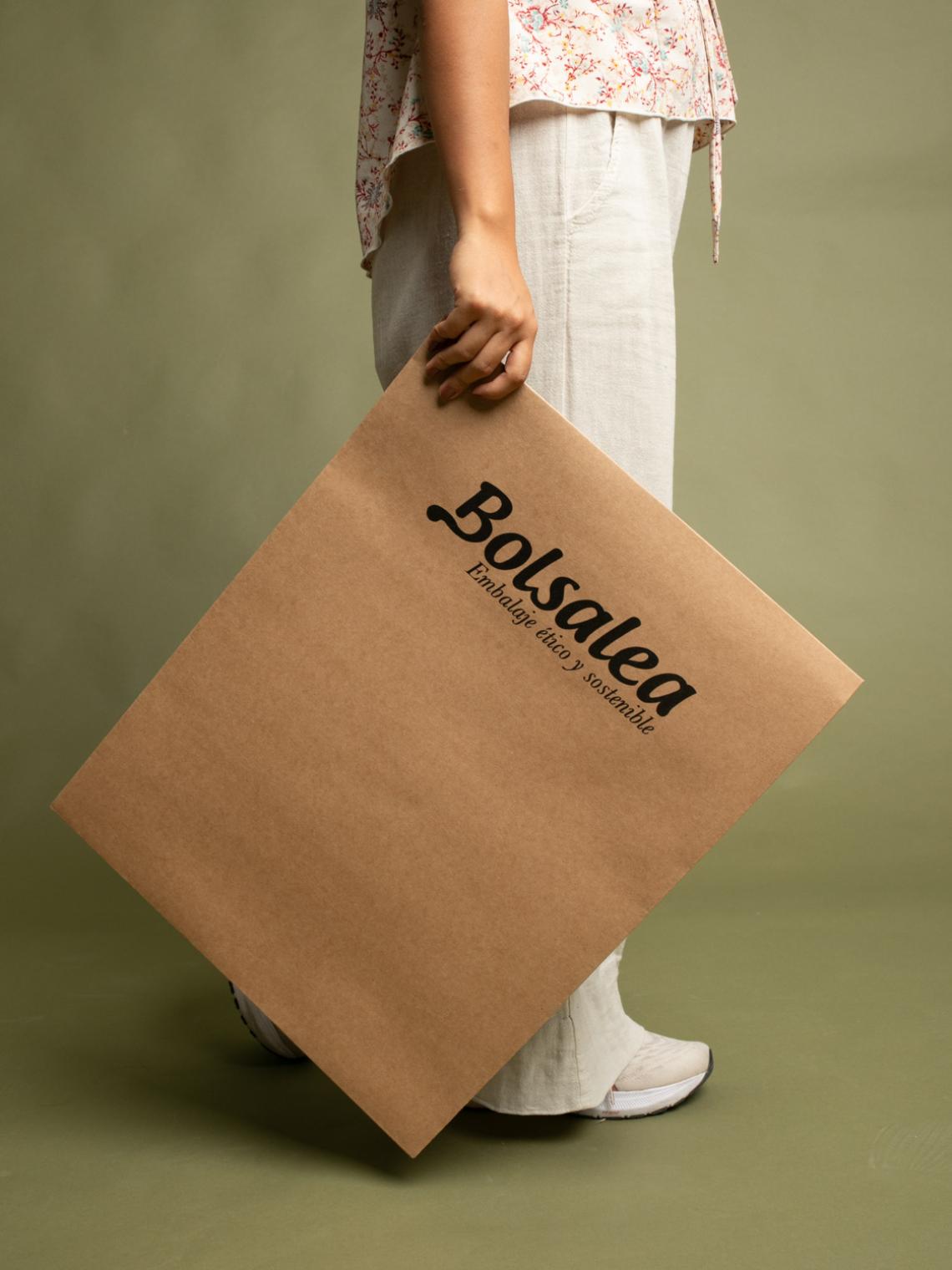 Persona de pie sosteniendo un sobre kraft grande con el logo de Bolsalea. Fabricado en España con materiales reciclables y empleo inclusivo.