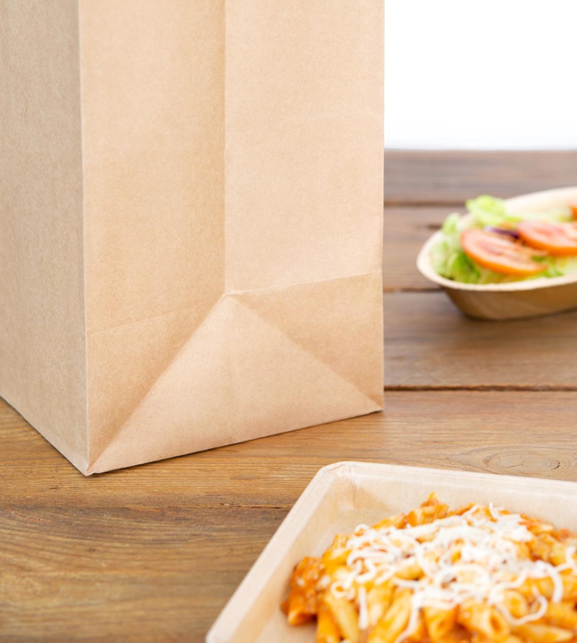 Bolsas grandes de papel reciclado take away junto a platos de comida