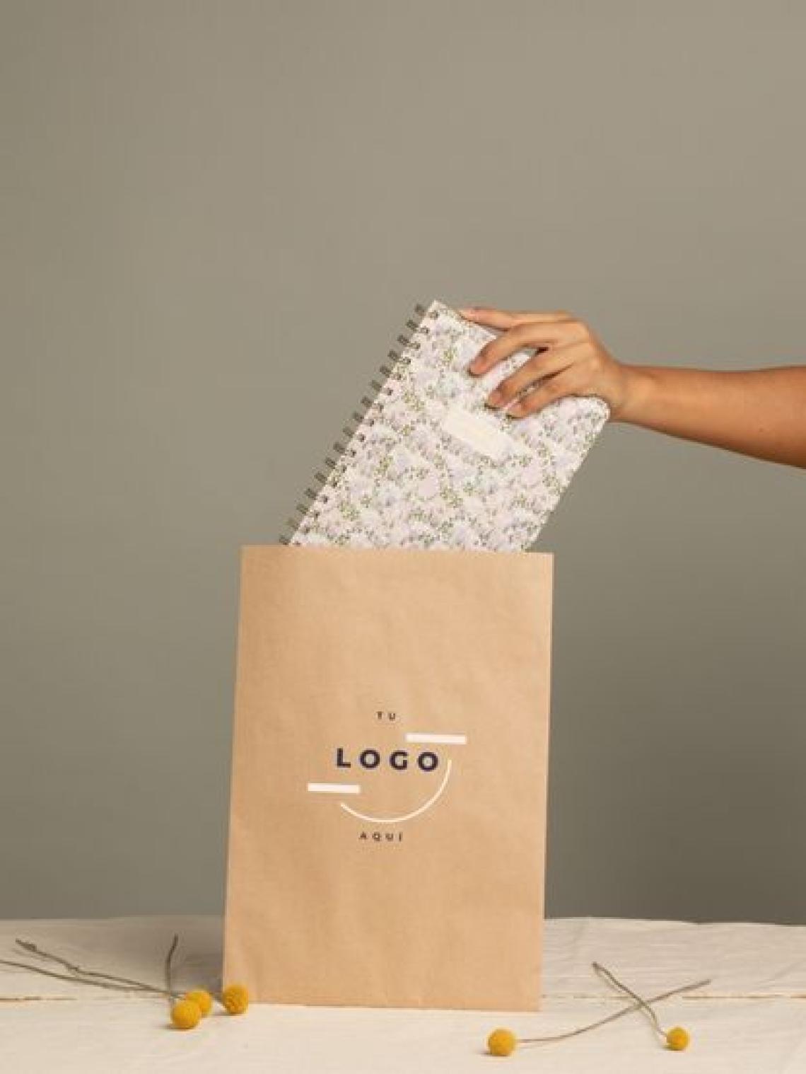 Mano introduciendo una libreta en un sobre de papel kraft reciclable y personalizable con logotipo