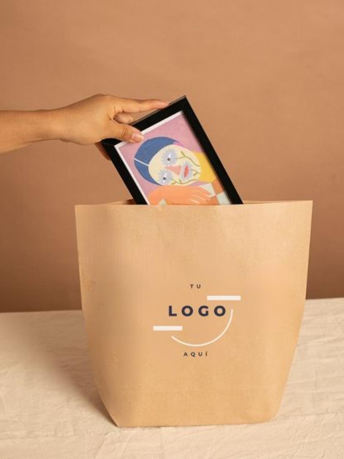 Mano introduciendo un marco con ilustración en una bolsa de papel kraft hexagonal grande personalizable con logotipo