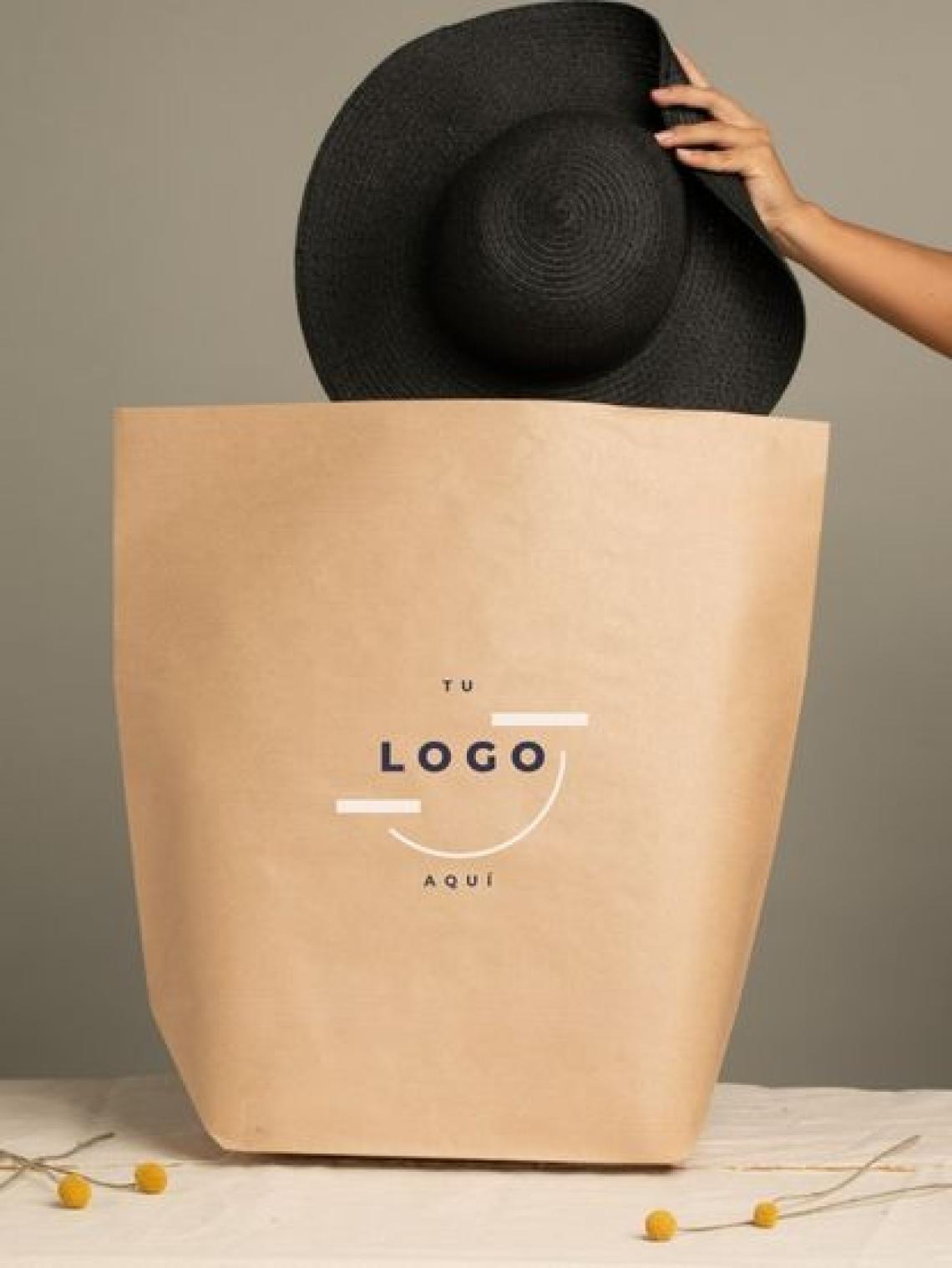 Mano colocando un sombrero negro en una bolsa de papel kraft hexagonal maxi sin asas, personalizable con logotipo y fabricada en España