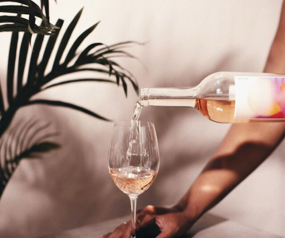 Aparecen unas manos echando vino a una copa