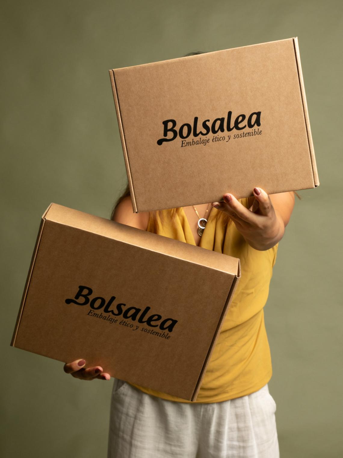 Persona sosteniendo dos cajas automontables de cartón kraft con el logo de Bolsalea. Embalaje ético y sostenible fabricado en España con materiales reciclables y empleo inclusivo. Si deseas tus cajas con separadores interiores, contáctanos.