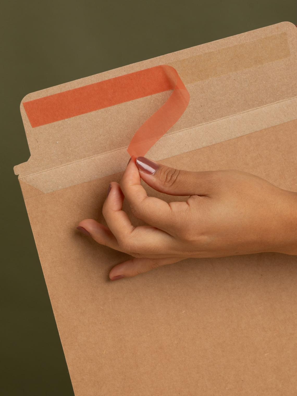 Detalle de sobre kraft con cierre adhesivo | Embalaje sostenible Bolsalea Mano retirando la cinta adhesiva de un sobre kraft reciclable de Bolsalea. Fabricado en España con impacto social y materiales ecológicos.