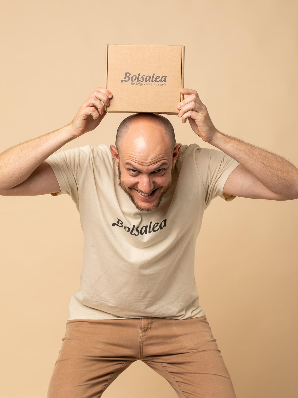 Caja automontable de cartón kraft pequeña | Packaging sostenible Bolsalea Persona sonriente sosteniendo sobre su cabeza una caja automontable de cartón kraft con el logo de Bolsalea. Embalaje ético y sostenible fabricado en España con impacto social. Si deseas tu caja con separadores interiores, contáctanos.