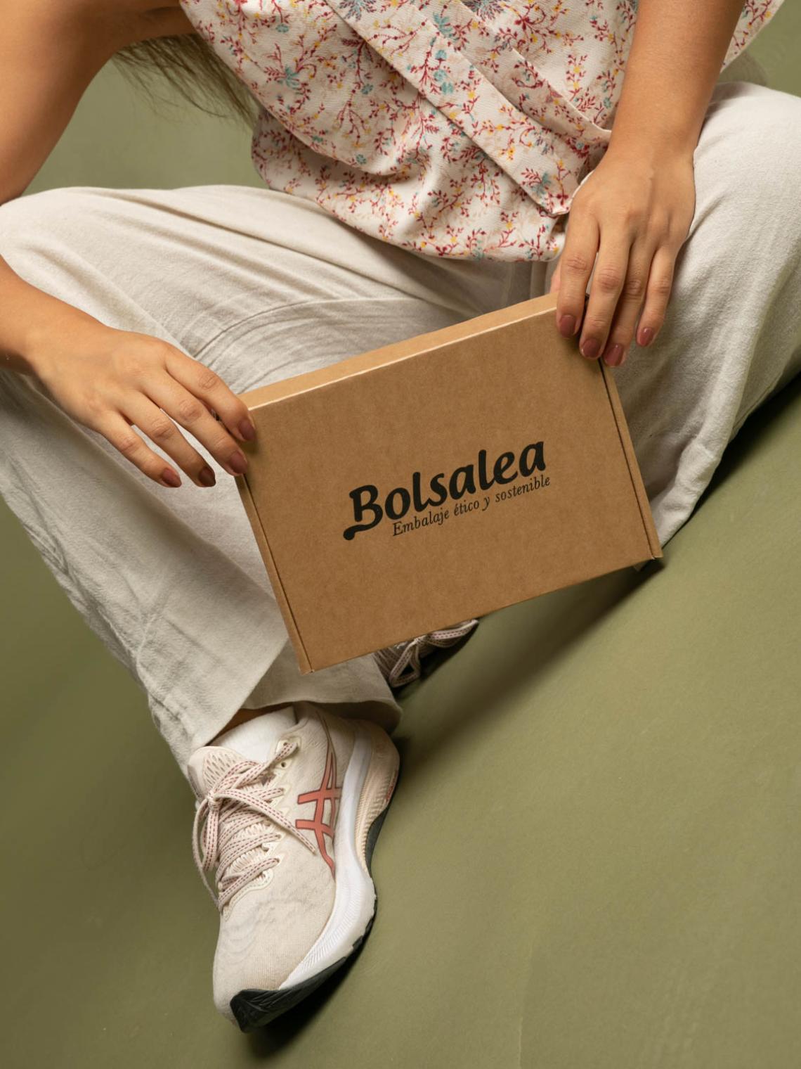 Persona sentada con una caja automontable de cartón kraft con el logo de Bolsalea. Embalaje ético y sostenible fabricado en España, ideal para envíos responsables y marcas conscientes.