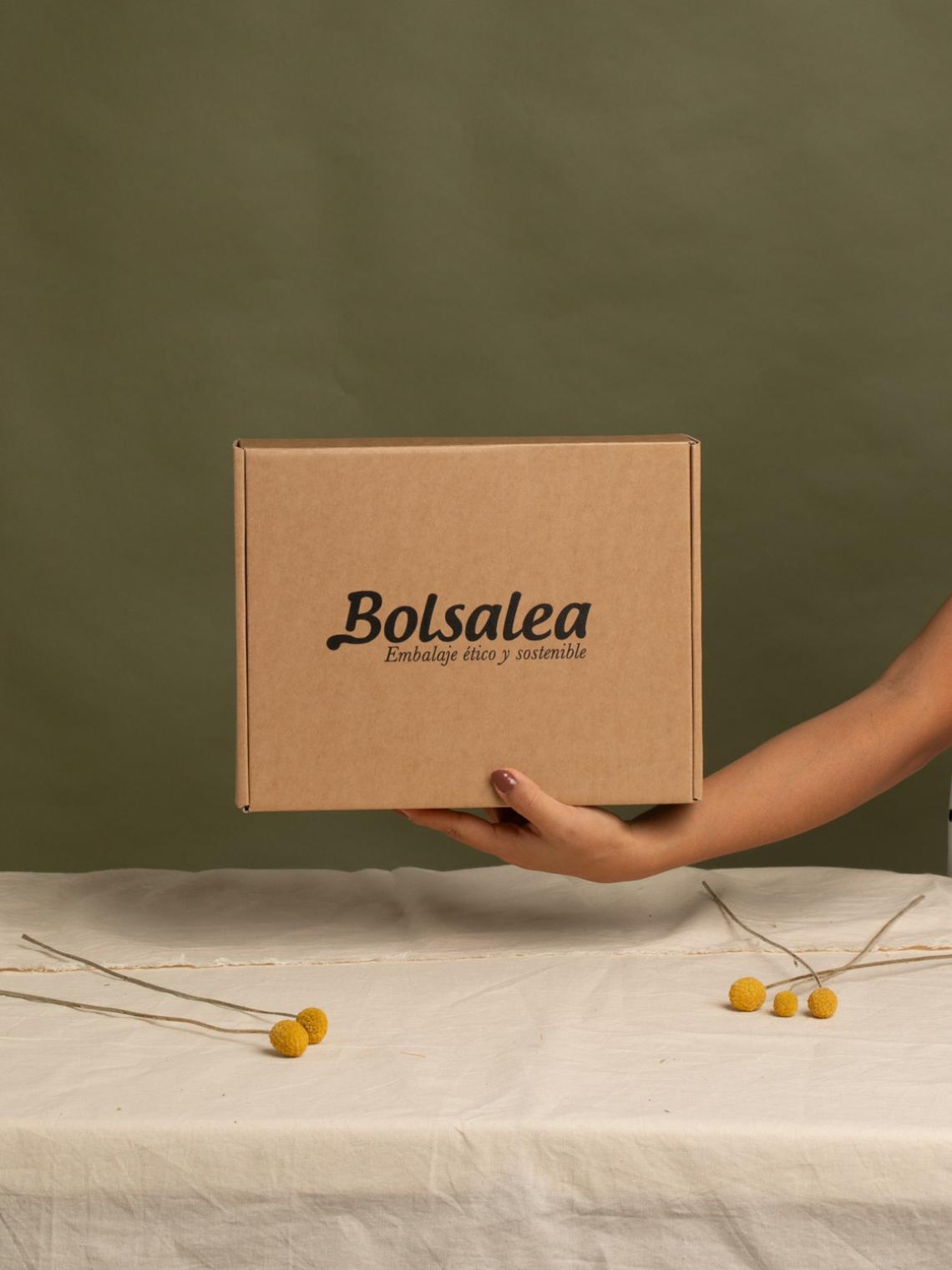 Mano sosteniendo una caja automontable de cartón kraft con el logo de Bolsalea y el lema “Embalaje ético y sostenible”. Fabricada en España con materiales reciclables y empleo inclusivo. Si deseas tu caja con separadores interiores, contáctanos.