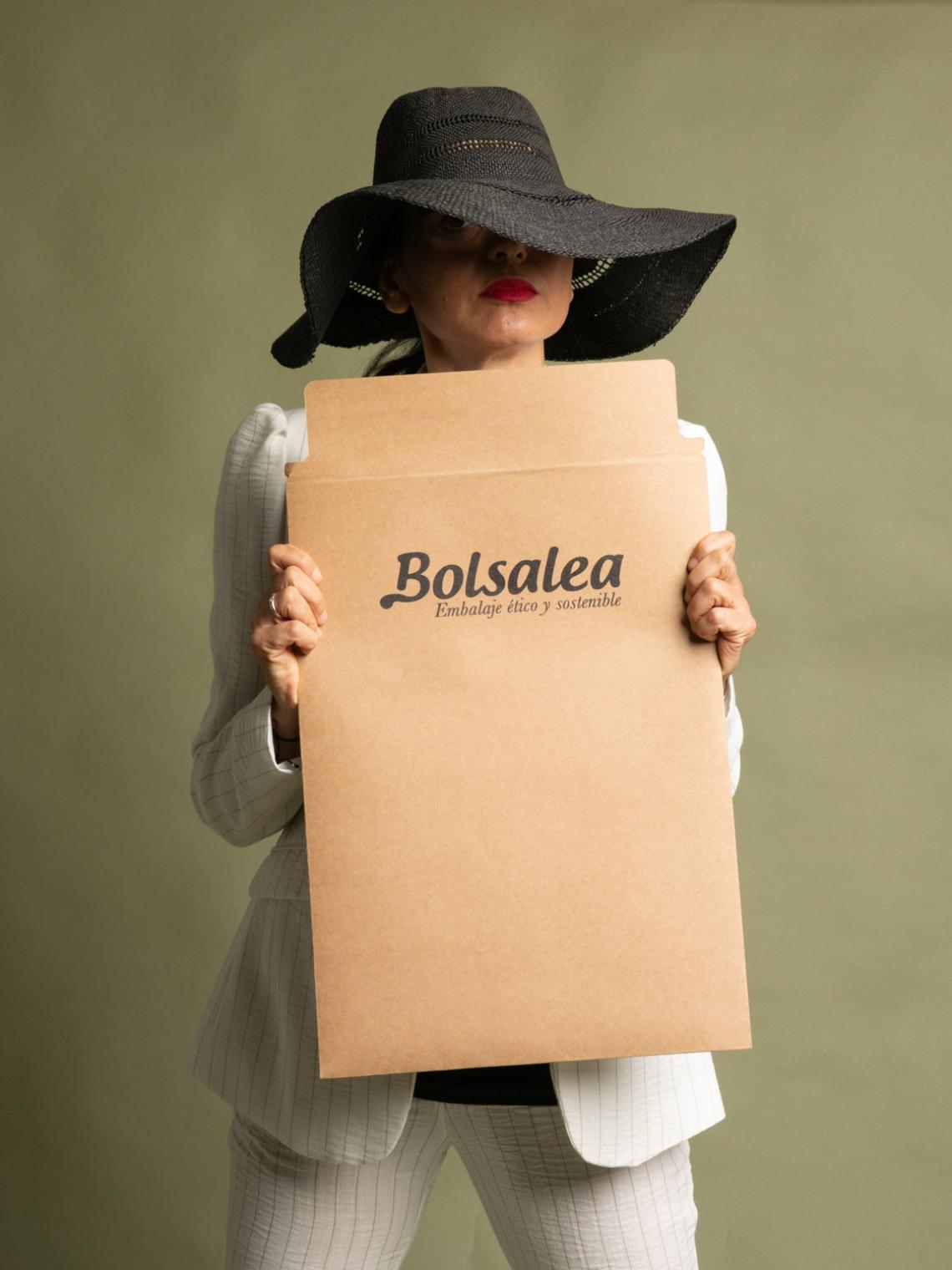 Sobre kraft grande para envíos responsables | Bolsalea Persona con sombrero sosteniendo un sobre kraft grande con el logo de Bolsalea. Embalaje ético y sostenible fabricado en España con impacto social.