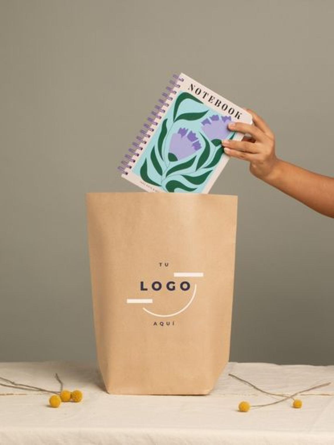 Mano introduciendo una libreta en una bolsa de papel kraft hexagonal grande sin asas, personalizable con logotipo y fabricada en España