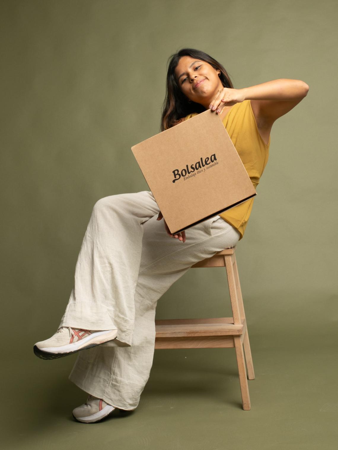 Persona sentada sujetando una caja automontable de cartón kraft con el logo de Bolsalea. Embalaje ético y sostenible fabricado en España con empleo inclusivo, ideal para envíos y packaging responsable.