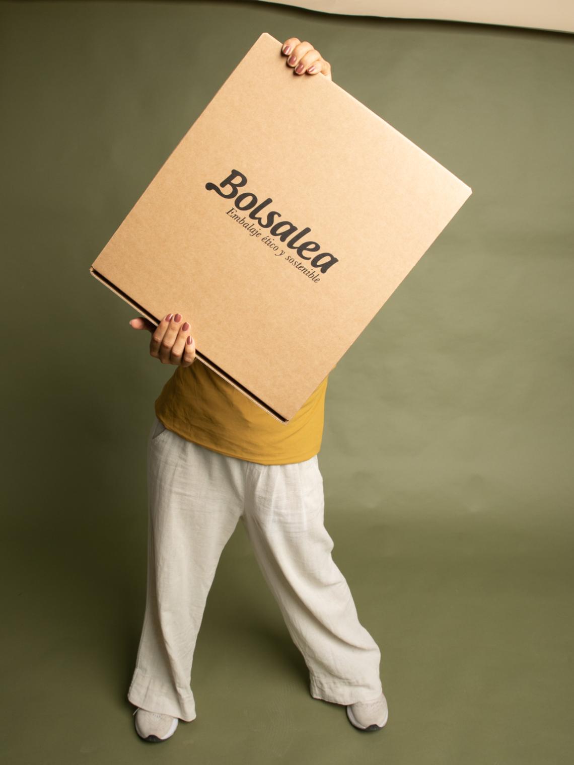 Caja automontable plana grande kraft | Fabricada en España con impacto social Persona sujetando una gran caja automontable de cartón kraft con el logo de Bolsalea. Embalaje ético, reciclable y hecho en España mediante empleo inclusivo.