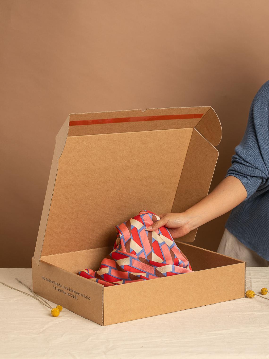 Caja automontable de cartón kraft abierta con una prenda de colores en su interior. Fabricada en España con materiales reciclables y empleo inclusivo por Bolsalea. Si deseas tu caja con separadores interiores, contáctanos.