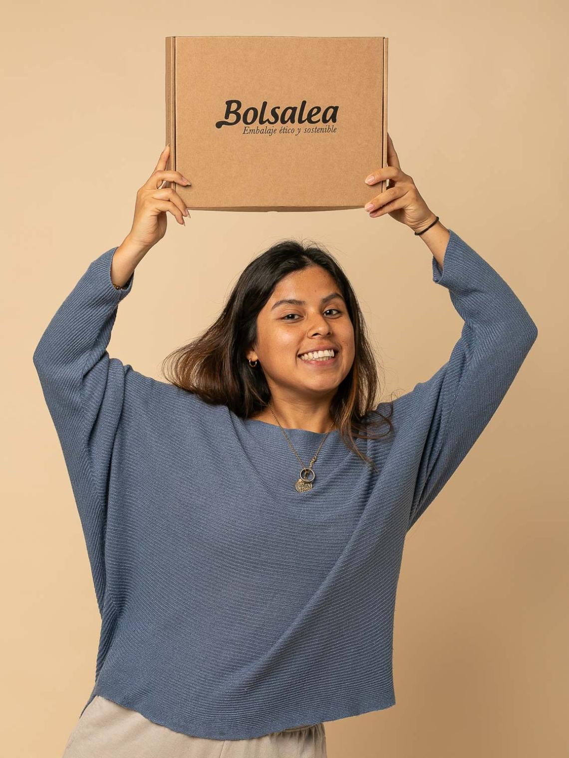 Persona sonriente sosteniendo sobre su cabeza una caja automontable de cartón kraft con el logo de Bolsalea. Embalaje ético y sostenible fabricado en España con impacto social. Si deseas tu caja con separadores interiores, contáctanos.