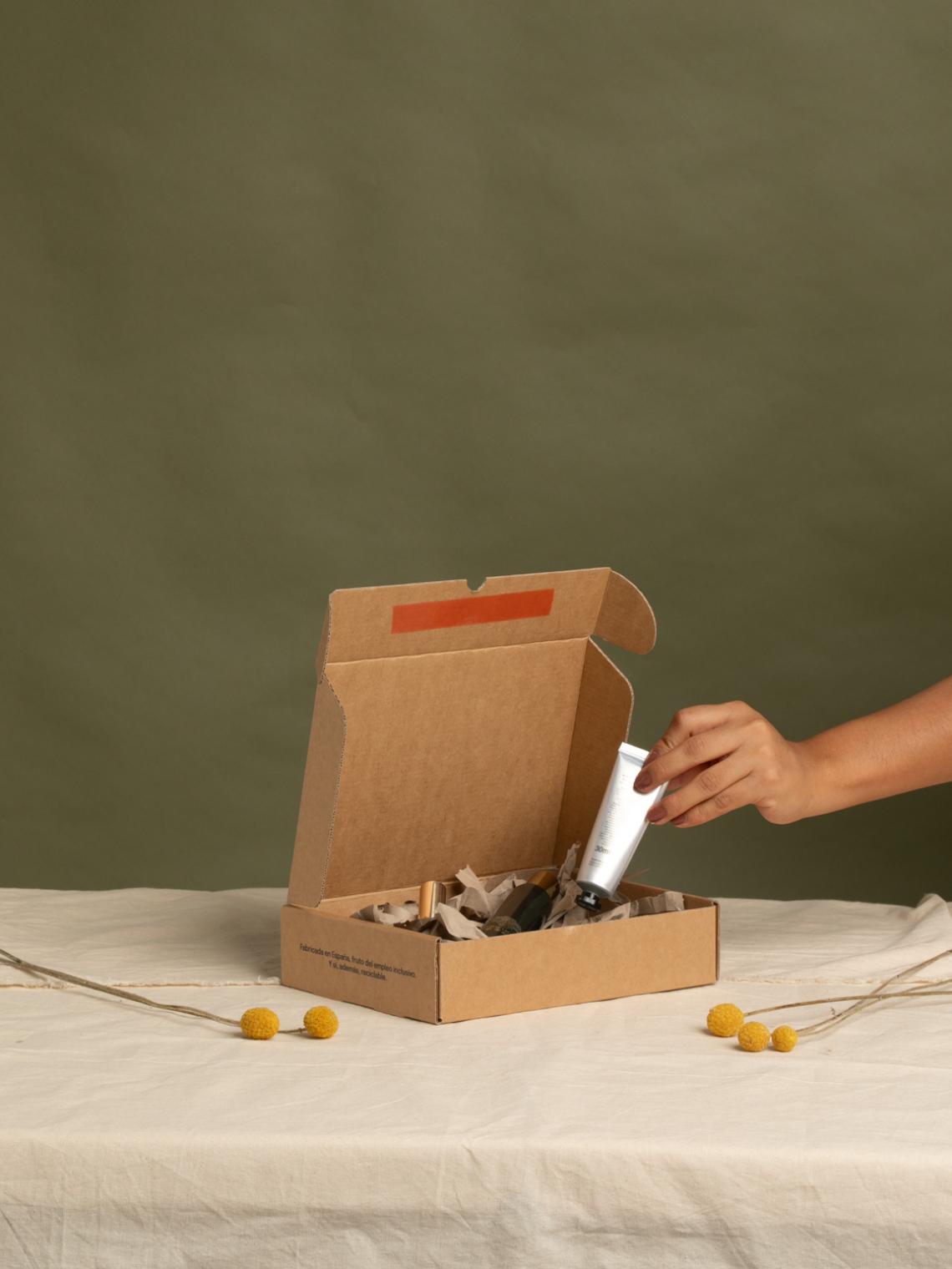 Caja automontable de cartón kraft con productos cosméticos en su interior, fabricada en España por Bolsalea con impacto social y materiales sostenibles. Ideal para packaging ecológico de ecommerce.