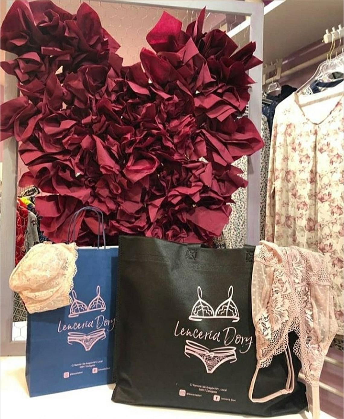 Bolsas de tela negras grandes con asas largas y fuelle en base junto a una bolsa de papel azul marino impresa