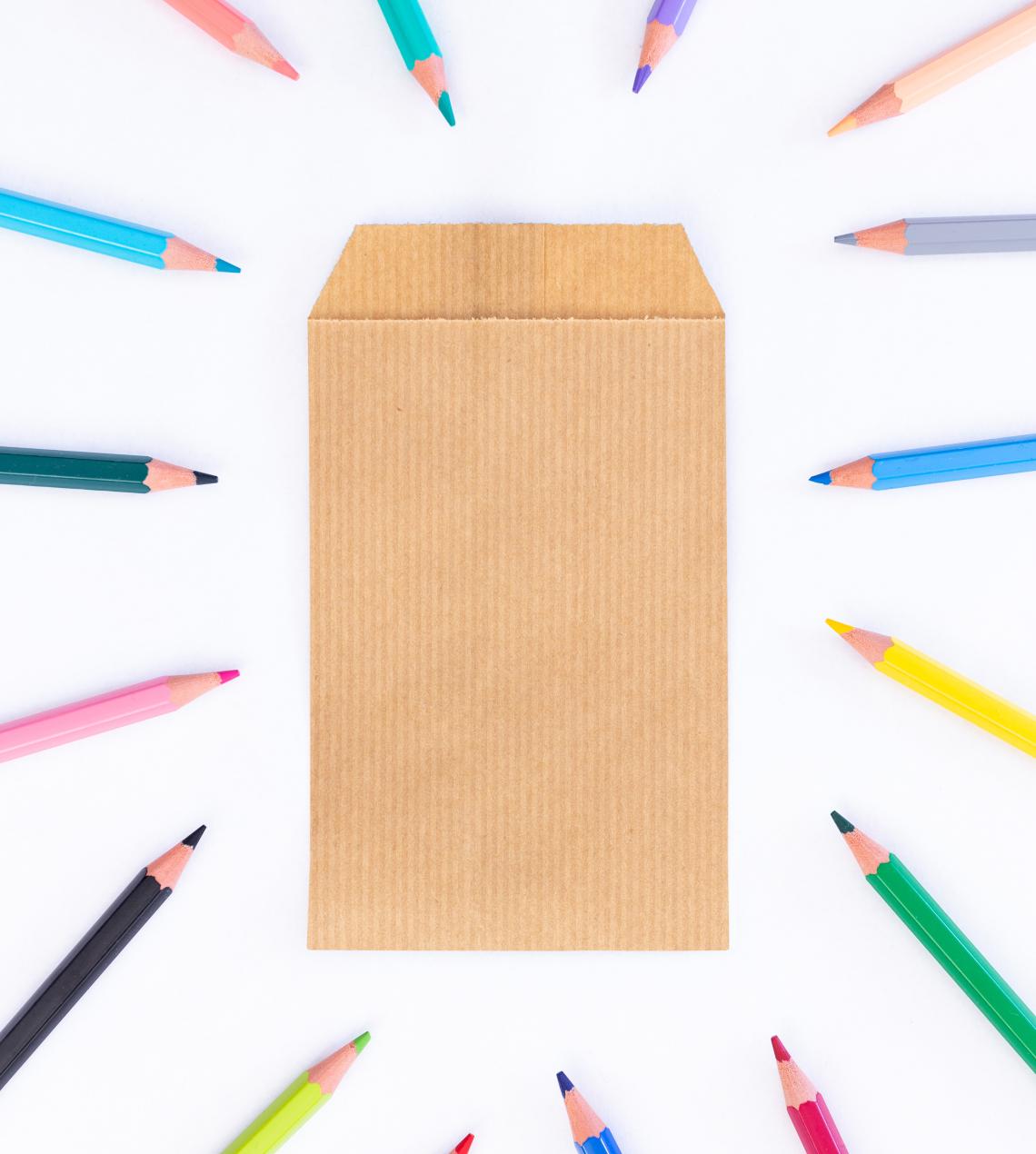 Sobres de papel pequeños kraft con lápices alrededor