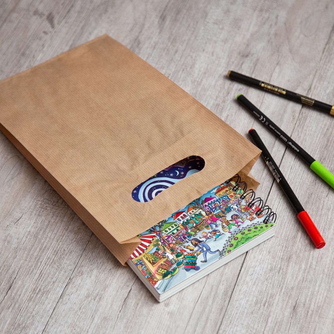 Bolsas de papel con asas troqueladas que tienen rotuladores a los lados y un cuaderno dentro