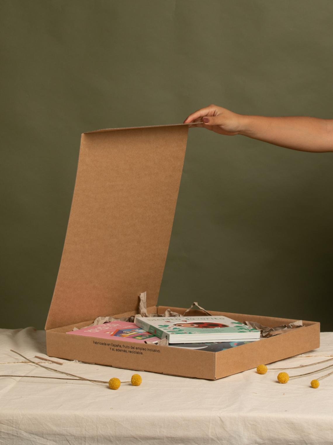 Caja automontable plana kraft con apertura superior | Hecha en España con empleo inclusivo Caja automontable de cartón kraft abierta con libros en su interior y relleno de papel reciclado. Fabricada en España por Bolsalea con impacto social y materiales reciclables.