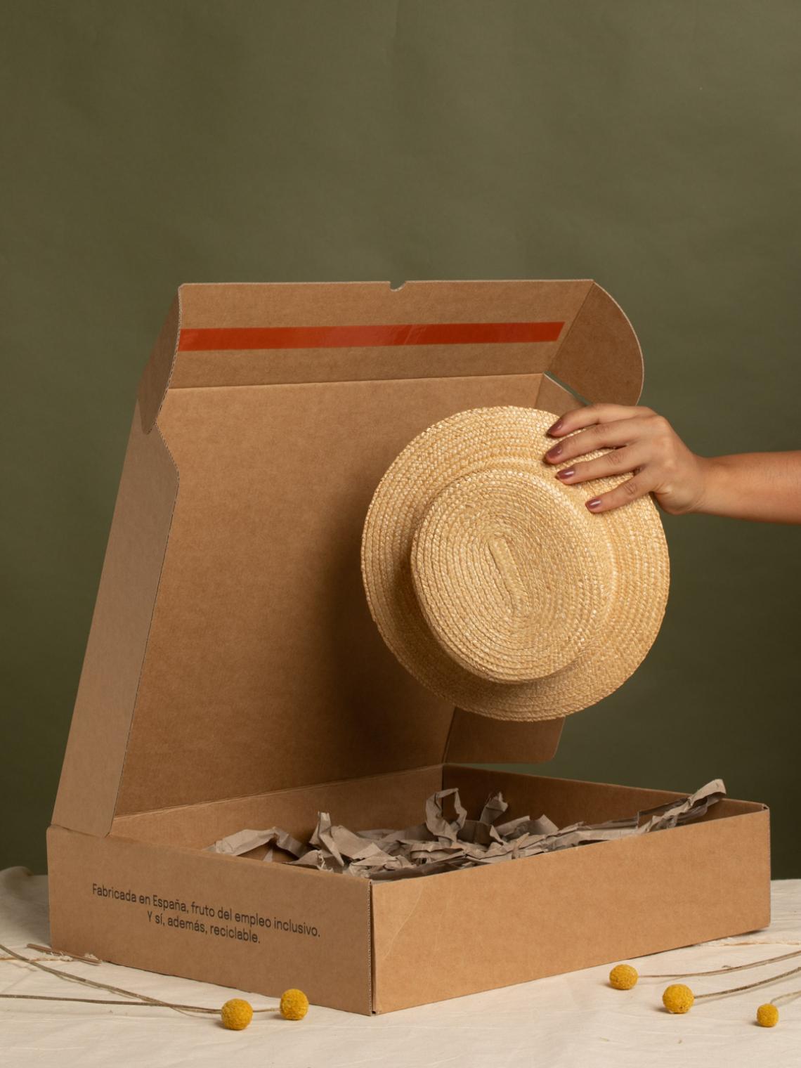 Caja automontable de cartón kraft abierta con relleno reciclado y un sombrero en su interior. Fabricada en España por Bolsalea con materiales reciclables y empleo inclusivo. Si deseas tu caja con separadores interiores, contáctanos.