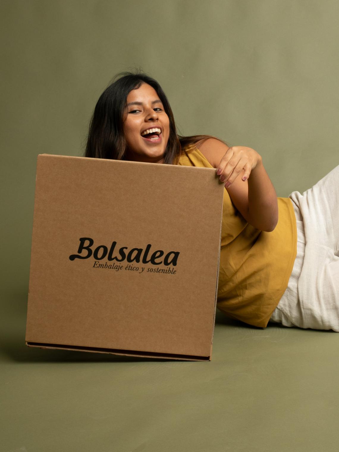 Persona tumbada sosteniendo una caja automontable de cartón kraft con el logo de Bolsalea. Embalaje ético y sostenible fabricado en España con empleo inclusivo y materiales reciclables.