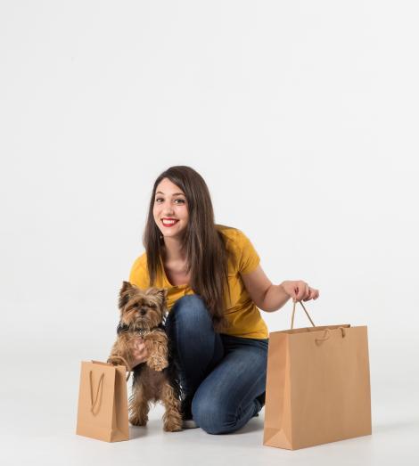 Bolsas de papel de lujo sujetas por una chica que además tiene en brazos a un perro